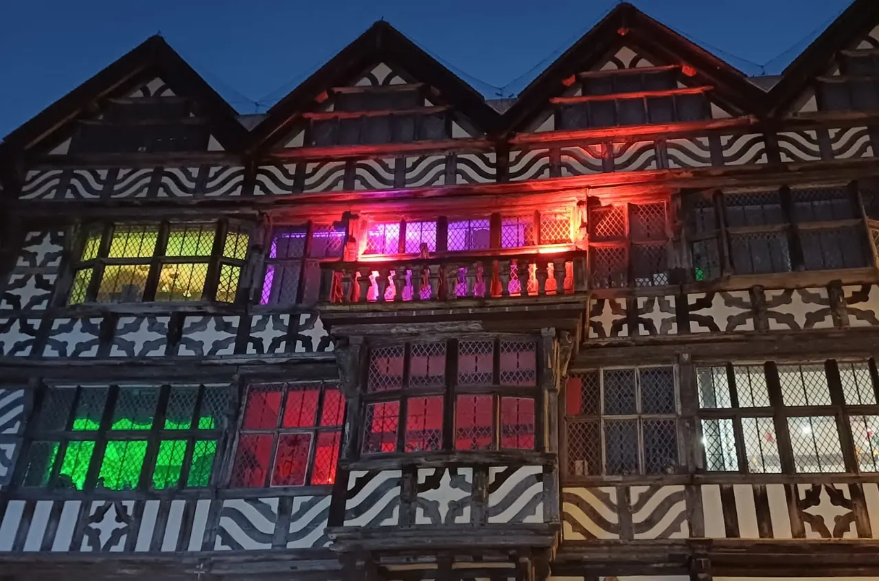 Historic timber-framed building illuminated at dusk with red, purple, and green neon lighting in windows.