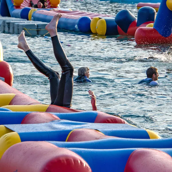 Person diving into water surrounded by colourful inflatable obstacle course buoys.