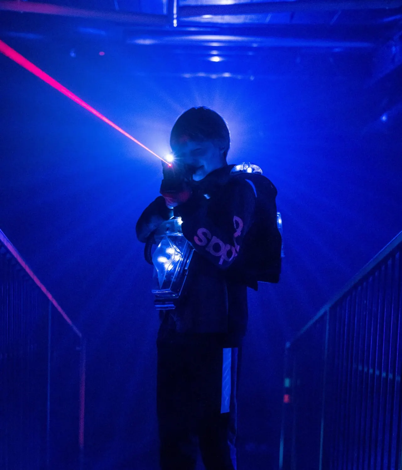 Player aiming laser tag gun in a dark multi-level arena
