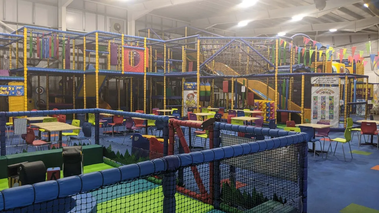 Indoor play centre with multiple soft play structures, climbing frames, slides and ball pits behind safety netting.