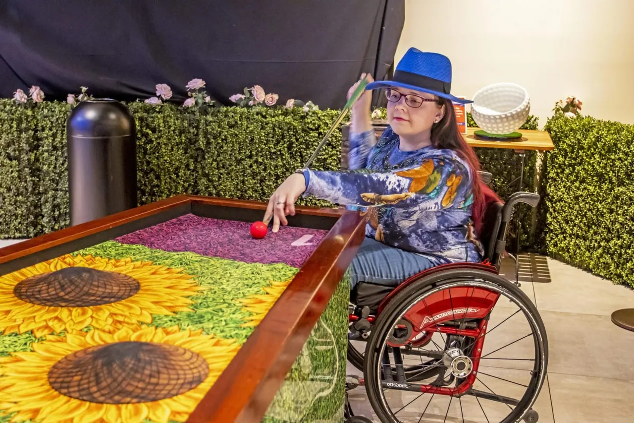Child in wheelchair playing putt-putt golf on a sunflower-themed course.