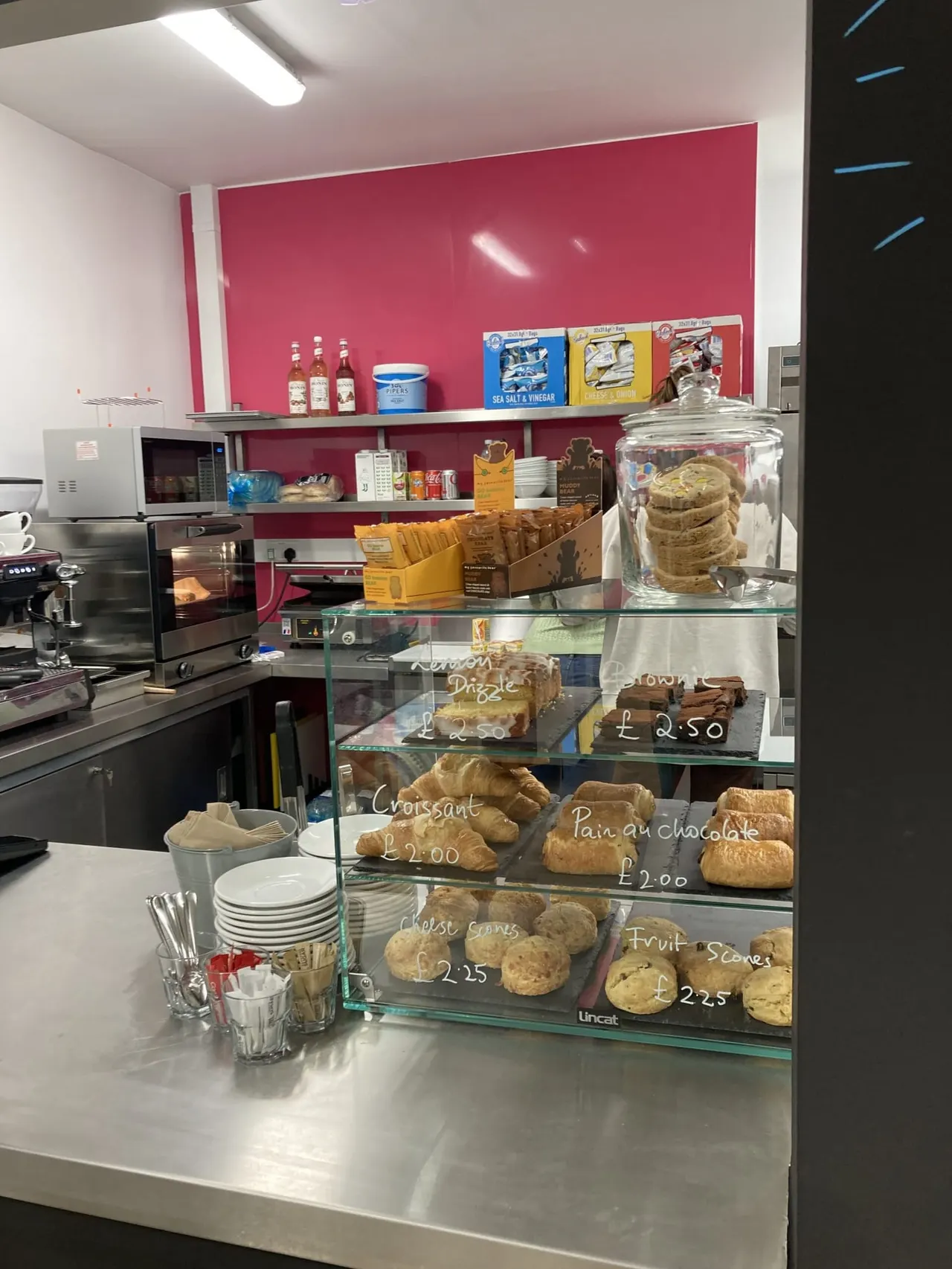 Glass display counter showcasing baked goods and pastries with price labels in a café setting.