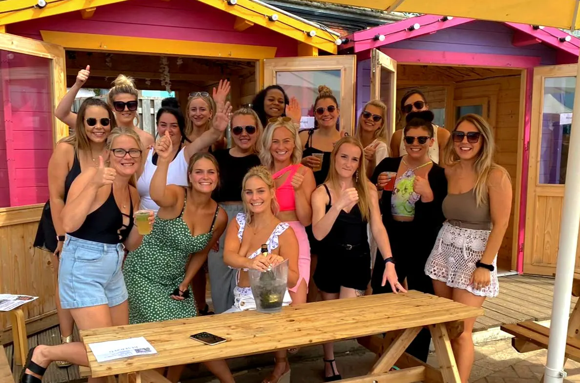 Large group of women posing together at an outdoor leisure venue with bright pink and yellow structural beams overhead.