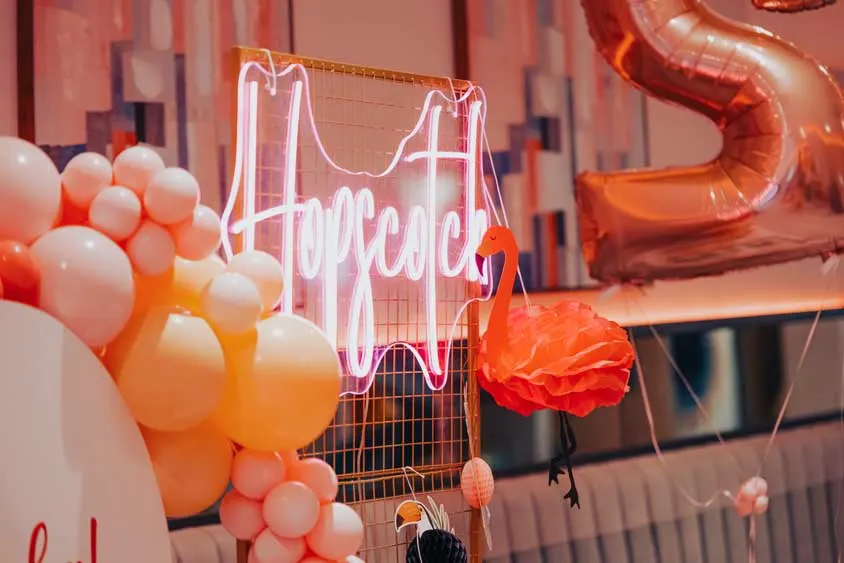 Neon sign and balloons in red, orange and white tones decorating an indoor celebration space.