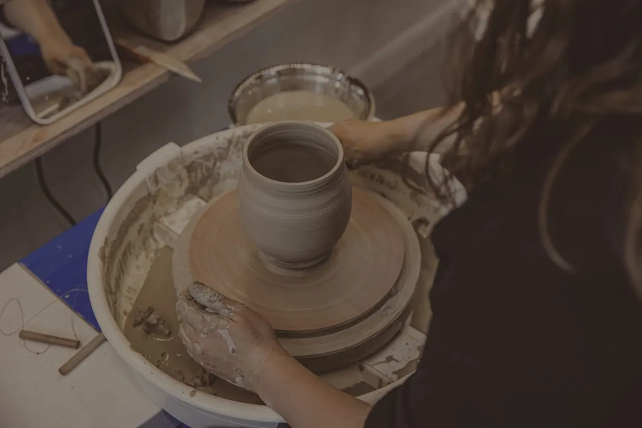 Person's hands shaping clay on a pottery wheel, creating a vessel with textured surface.
