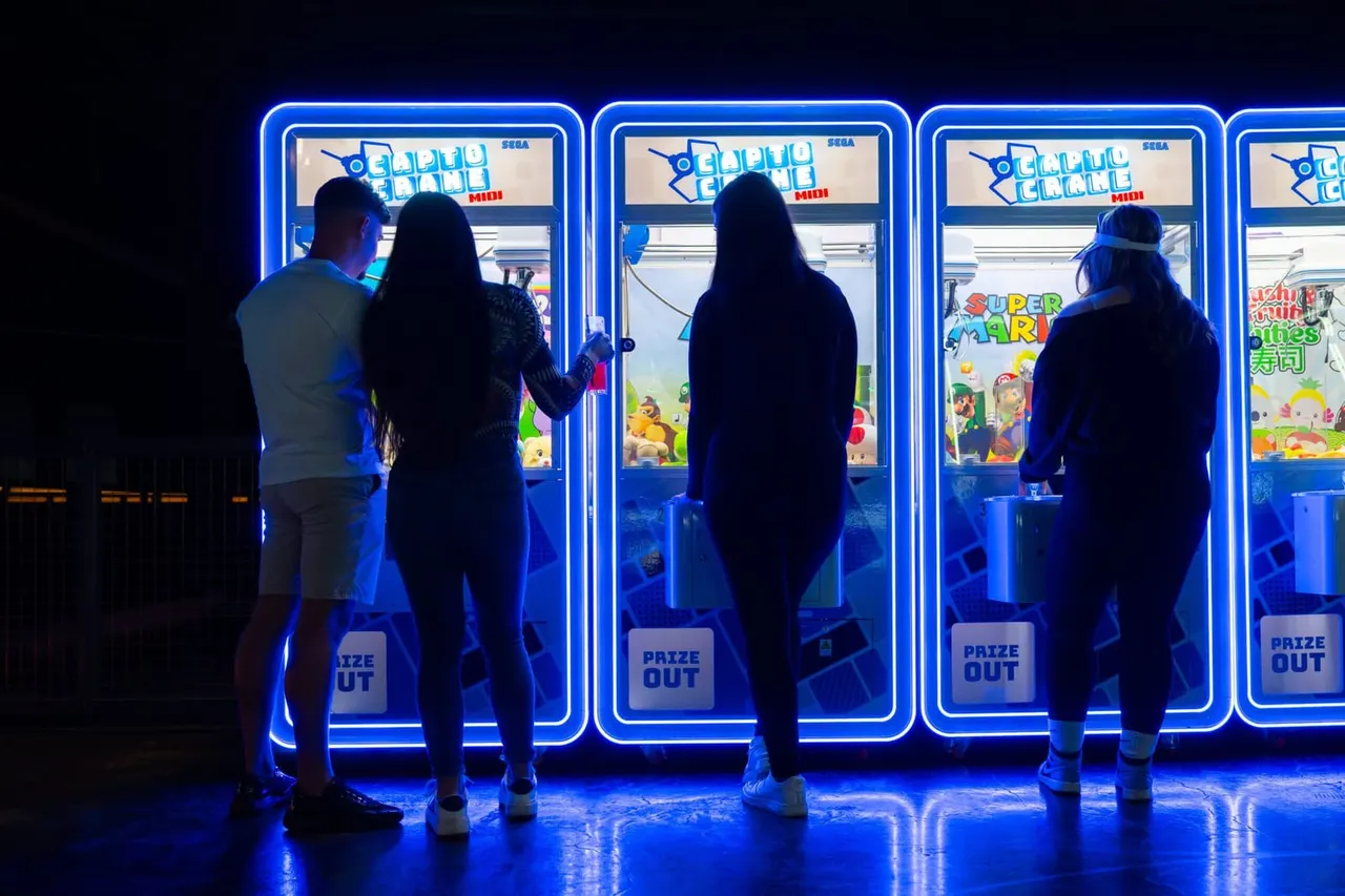 People playing at illuminated arcade games with blue neon frames in a dark venue.