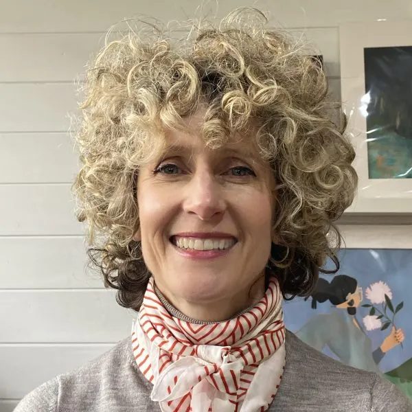 This is a photograph, so I'll describe what it shows:

Smiling woman with curly blonde hair wearing a red and white patterned scarf, indoors.