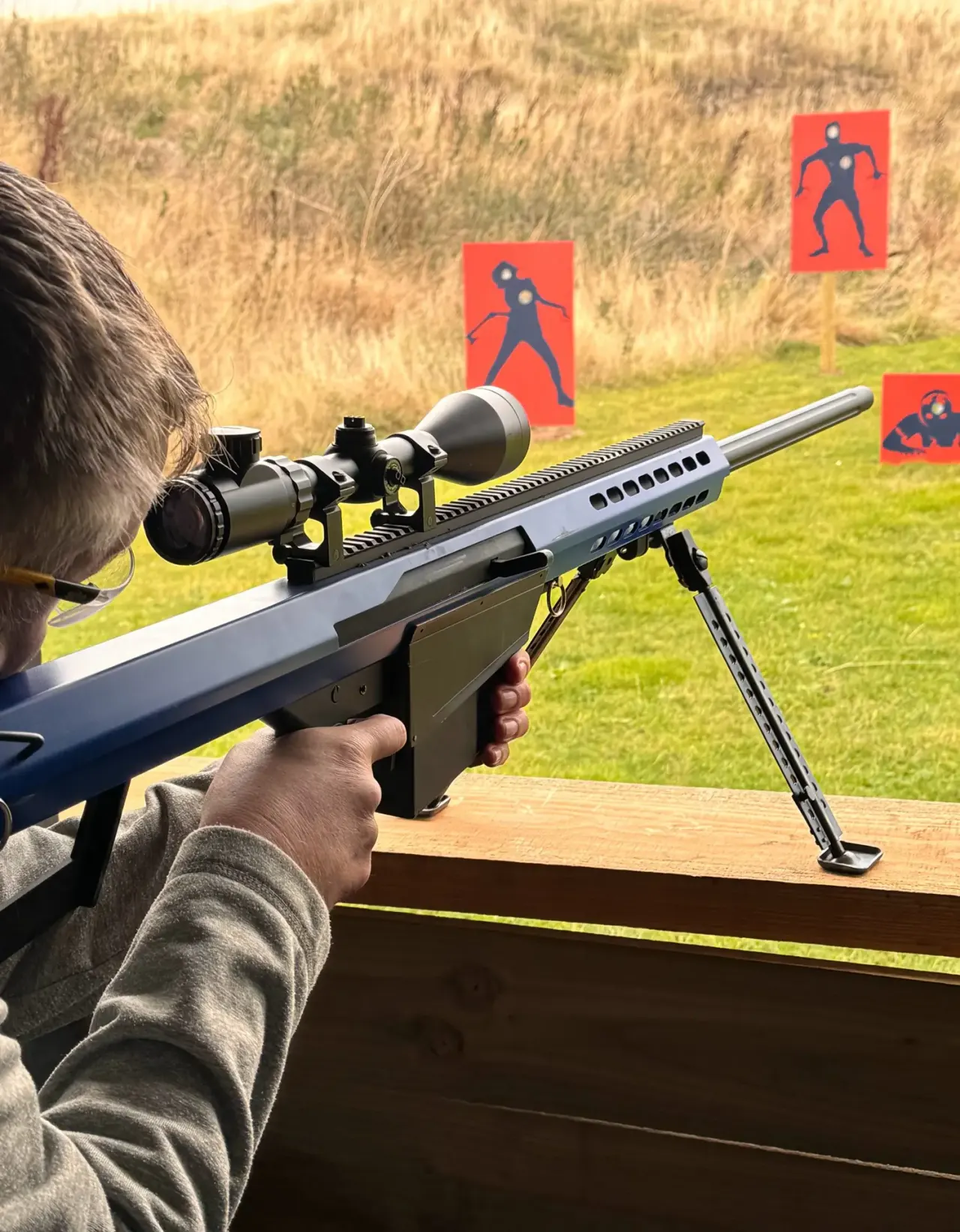 A person aiming a rifle with scoped sight at red silhouette targets on a grassy range.