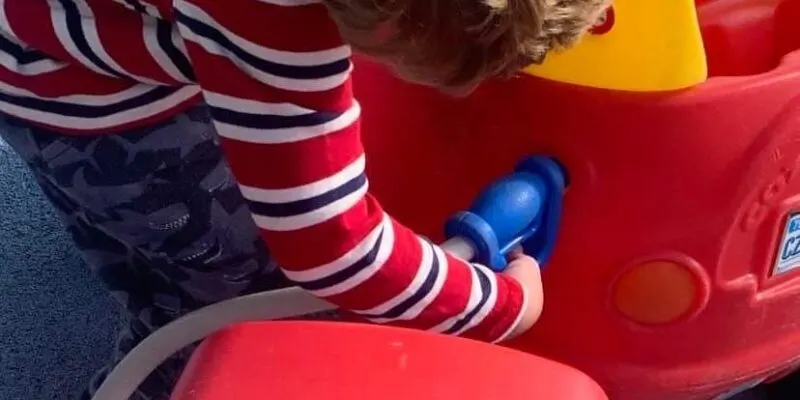 Child in striped socks sitting in a red ride-on toy car.