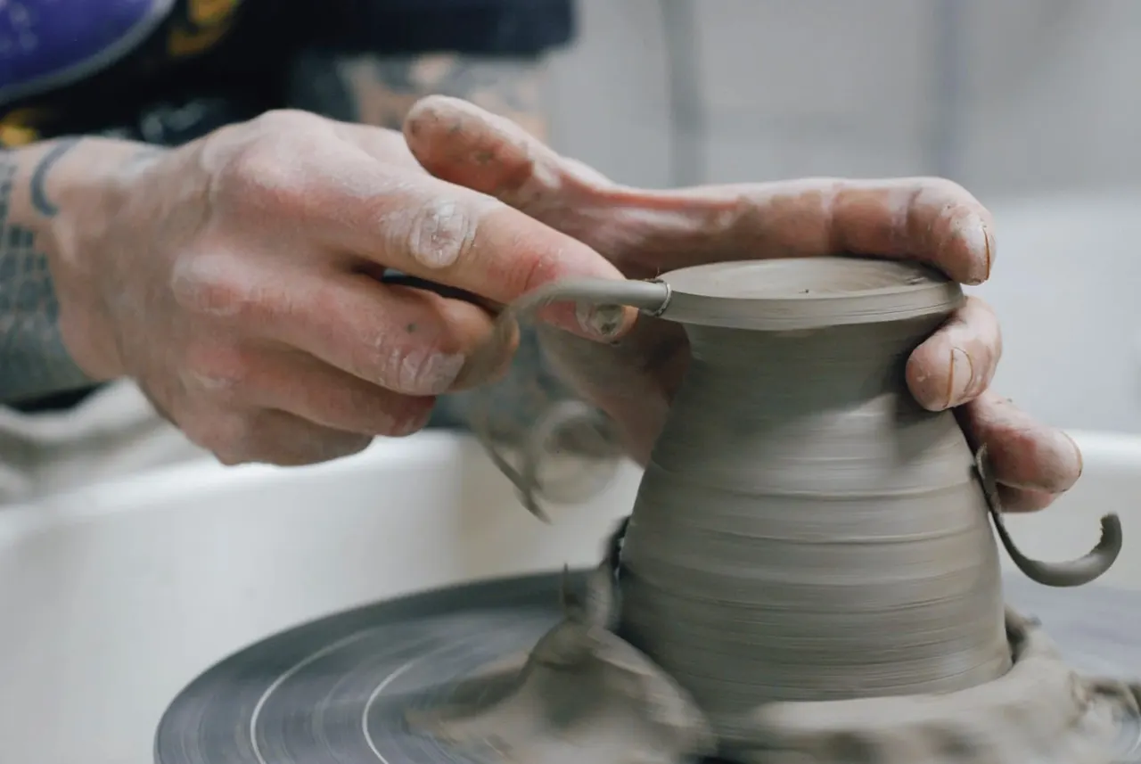 Pottery maker shaping wet clay on a spinning wheel to form a vessel.