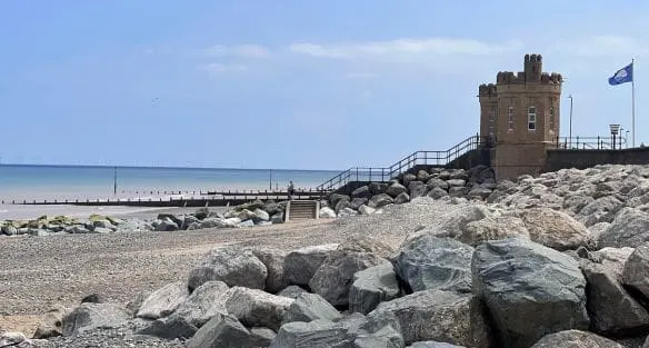 Stone breakwater and beach with historic brick tower building on rocky shore.