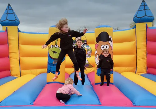 Young children playing and jumping on a large inflatable bouncy castle with character designs.