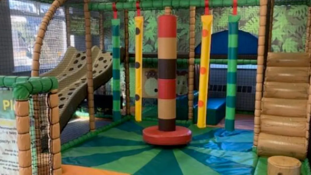 Indoor soft play area with colourful climbing poles, padded obstacles and wooden structures for children.