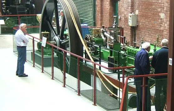 Visitors examining a large green industrial steam engine and machinery at an indoor museum display.