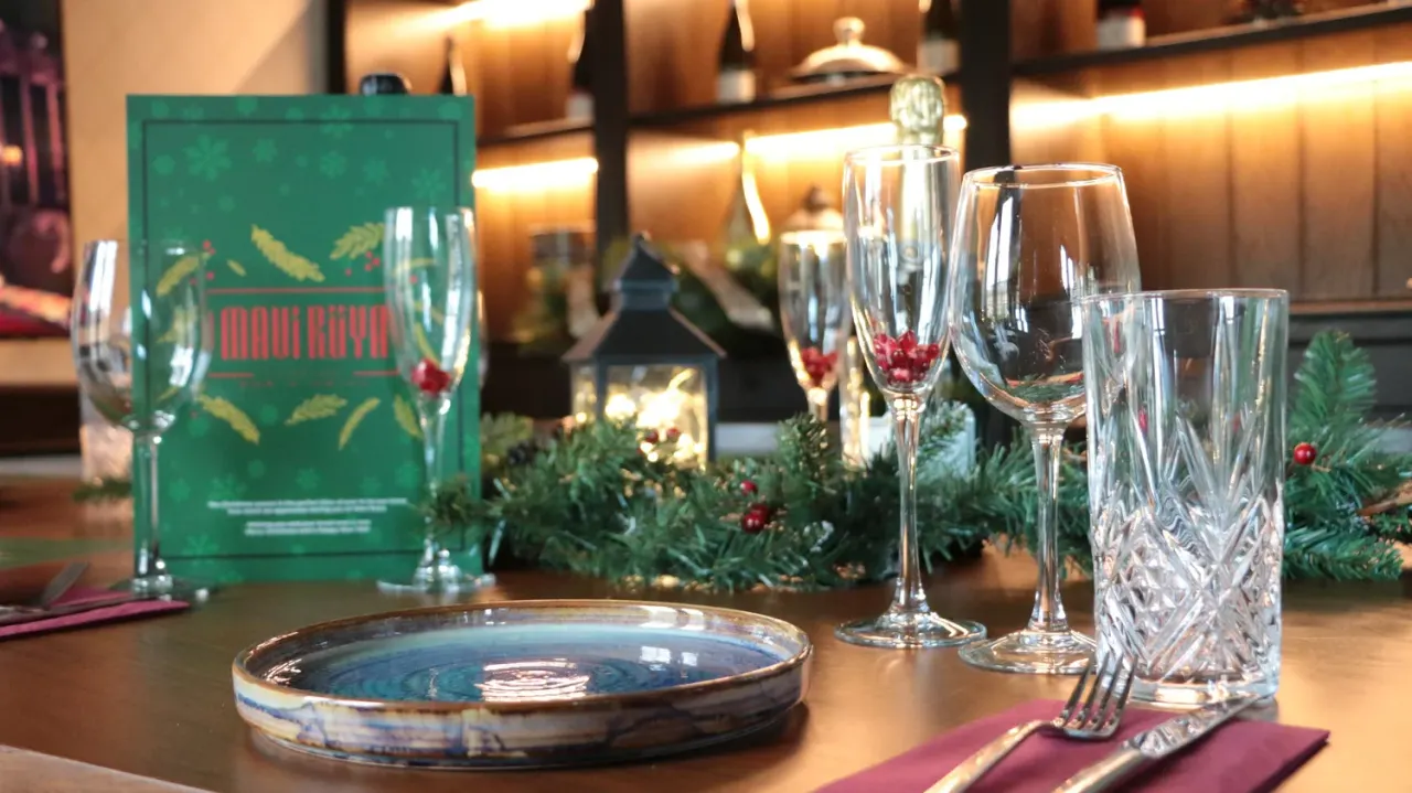 Elegantly set dining table with blue plate, glassware, festive greenery and red berries, and a green menu card.