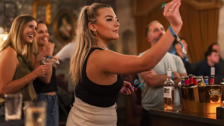 A woman takes a selfie whilst standing at a bar surrounded by guests enjoying drinks and socialising indoors.