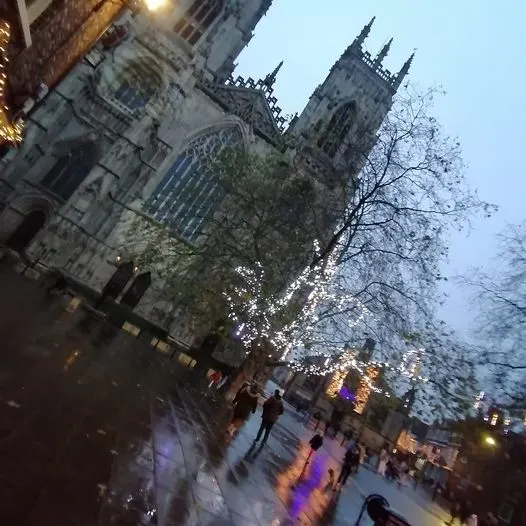 PHOTOGRAPH

Dusk view of York Minster with visitors walking through an illuminated street below the Gothic cathedral towers.