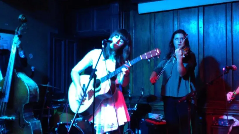 Band performing on stage with guitarist and singer under blue and red stage lighting.