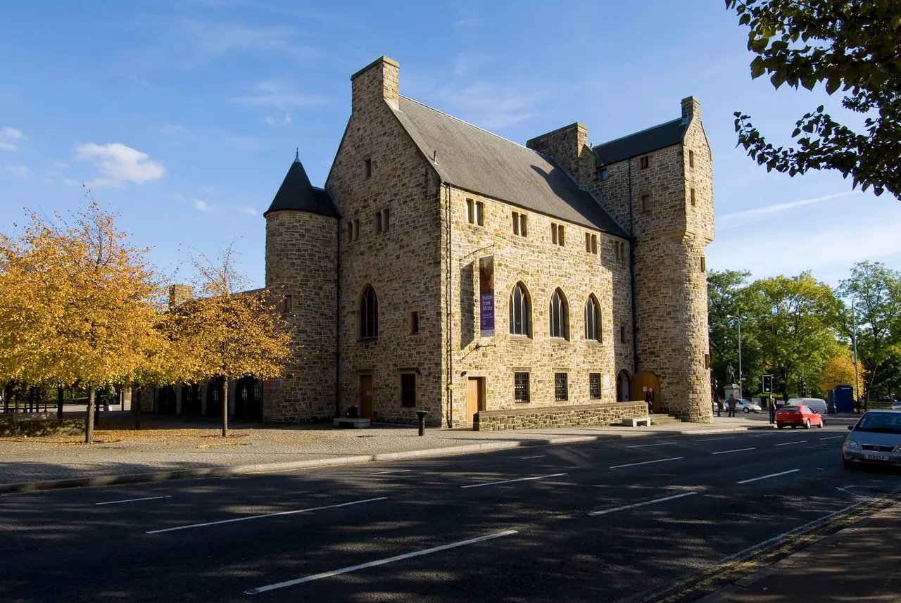 Historic stone building with turrets and tall windows facing a street, surrounded by autumn trees.