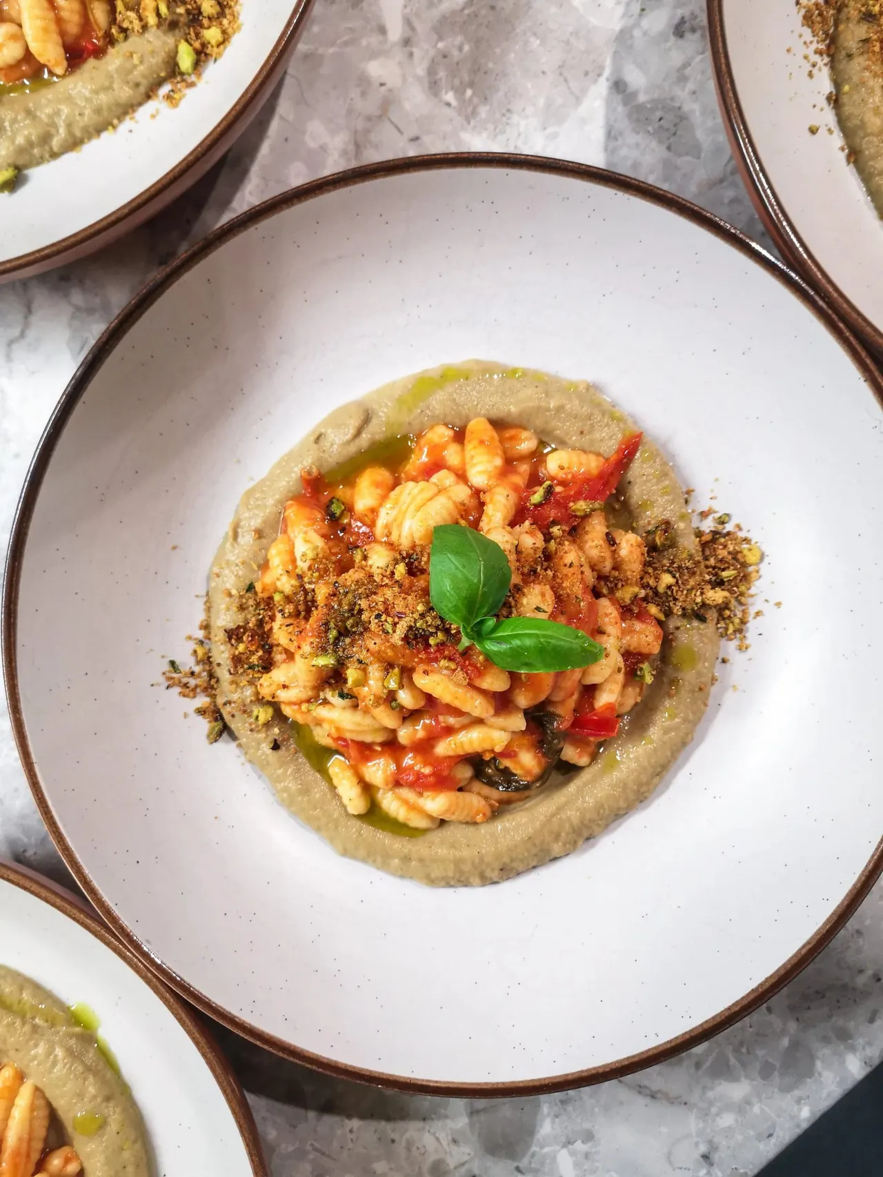 Hummus base topped with spiced prawns, red peppers and fresh basil on a white plate.