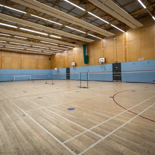 Empty sports hall with wooden floor, blue dividing panels, and fluorescent lighting.