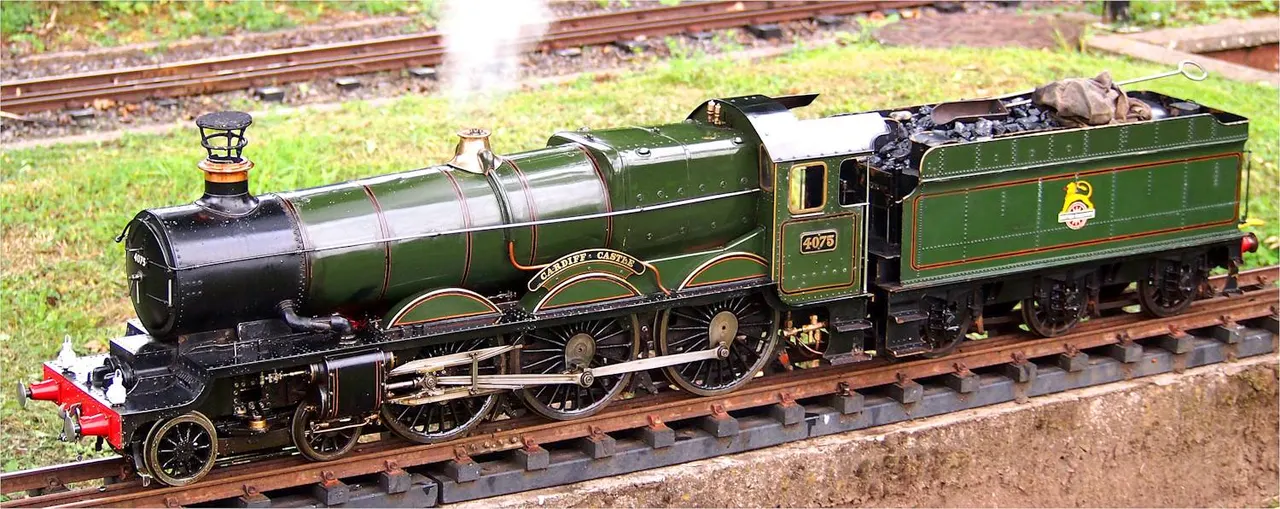Model steam locomotive and tender on miniature railway track with grass background.