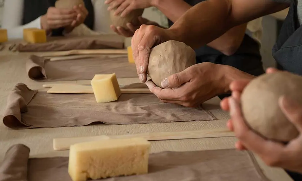 Group of people working with clay and tools at a pottery workshop table.
