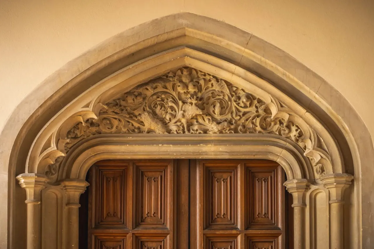 Ornate stone archway with decorative carved spandrel above wooden panelled doors.