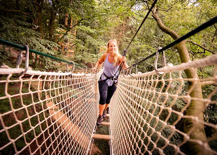 A woman running across a suspended rope bridge through a woodland canopy course.