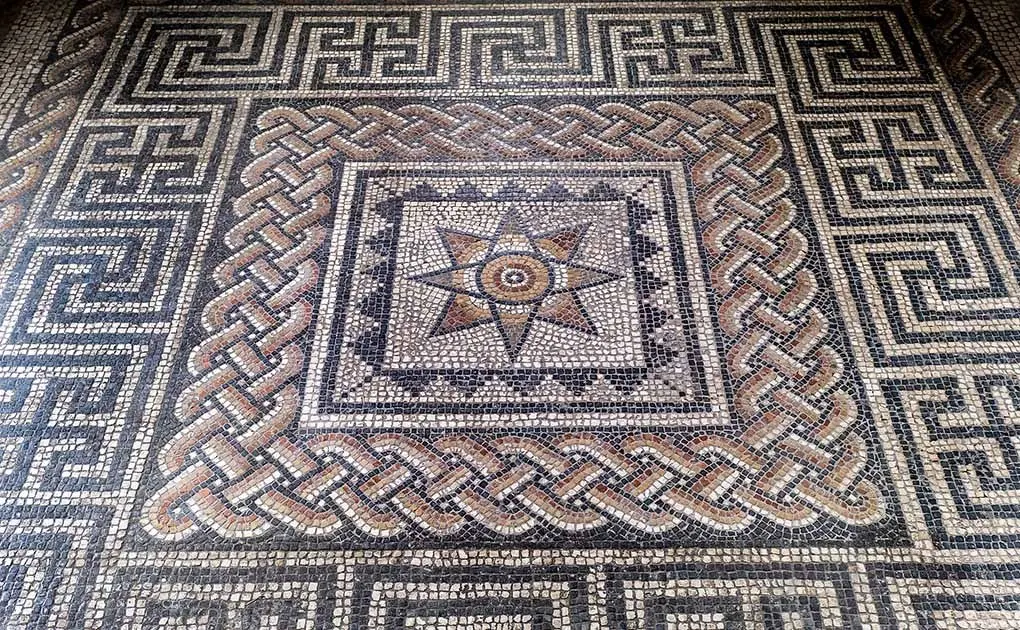 Ancient Roman mosaic floor with geometric patterns and central medallion design in terracotta and stone tesserae.