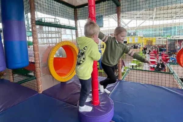 Two young children playing in an indoor soft play area with climbing equipment and obstacles.