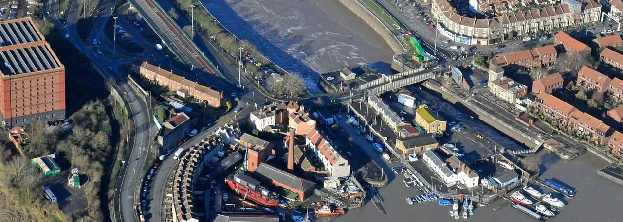 Aerial view of a waterside town district with moored boats, historic buildings, and a canal or river running through residential and commercial areas.