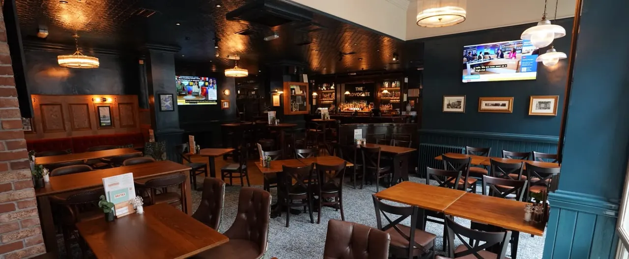 Upscale restaurant interior with wooden tables, leather chairs, dark blue walls, pendant lighting, and a bar counter at the back.