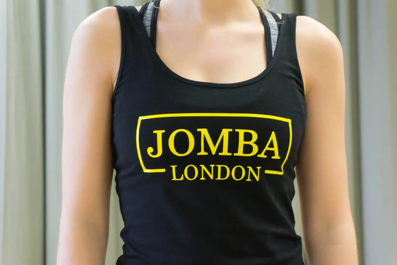 Person wearing black sports vest with yellow "JOMBA LONDON" logo print.