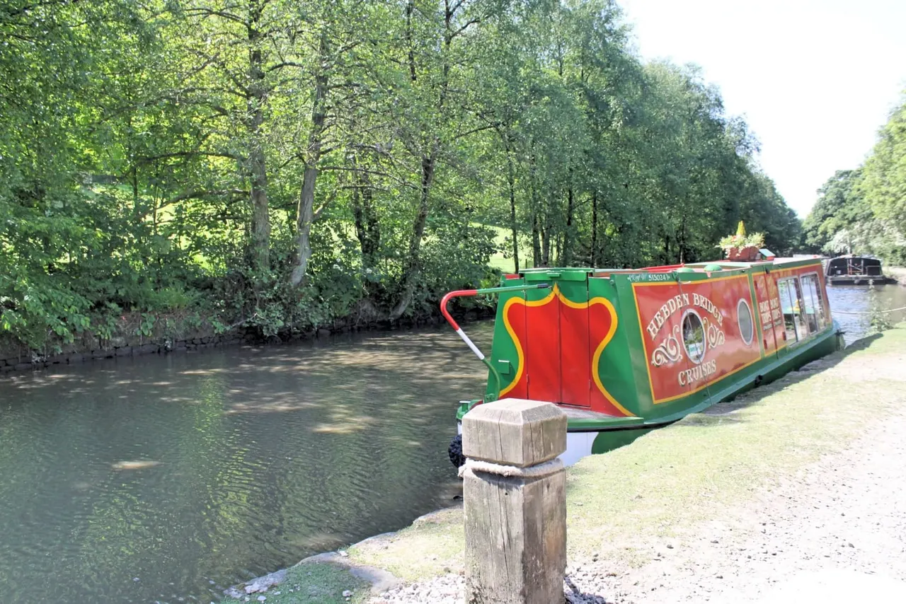 Colourful narrowboat moored on a canal beneath overhanging trees, with a wooden post in the foreground.