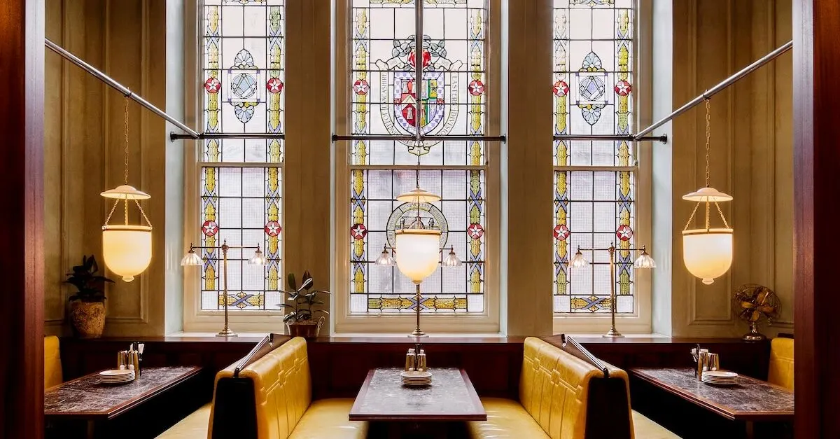 Upmarket restaurant dining room with booth seating, ornate stained-glass windows and hanging brass pendant lights.