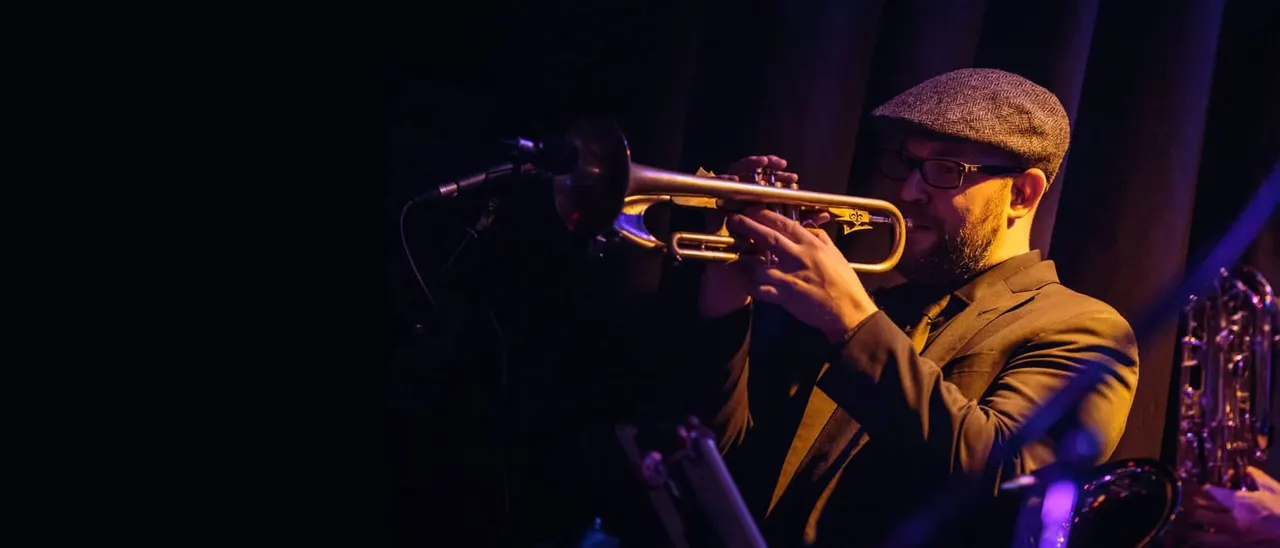 Musician playing trumpet on stage under purple and golden stage lighting during a live performance.