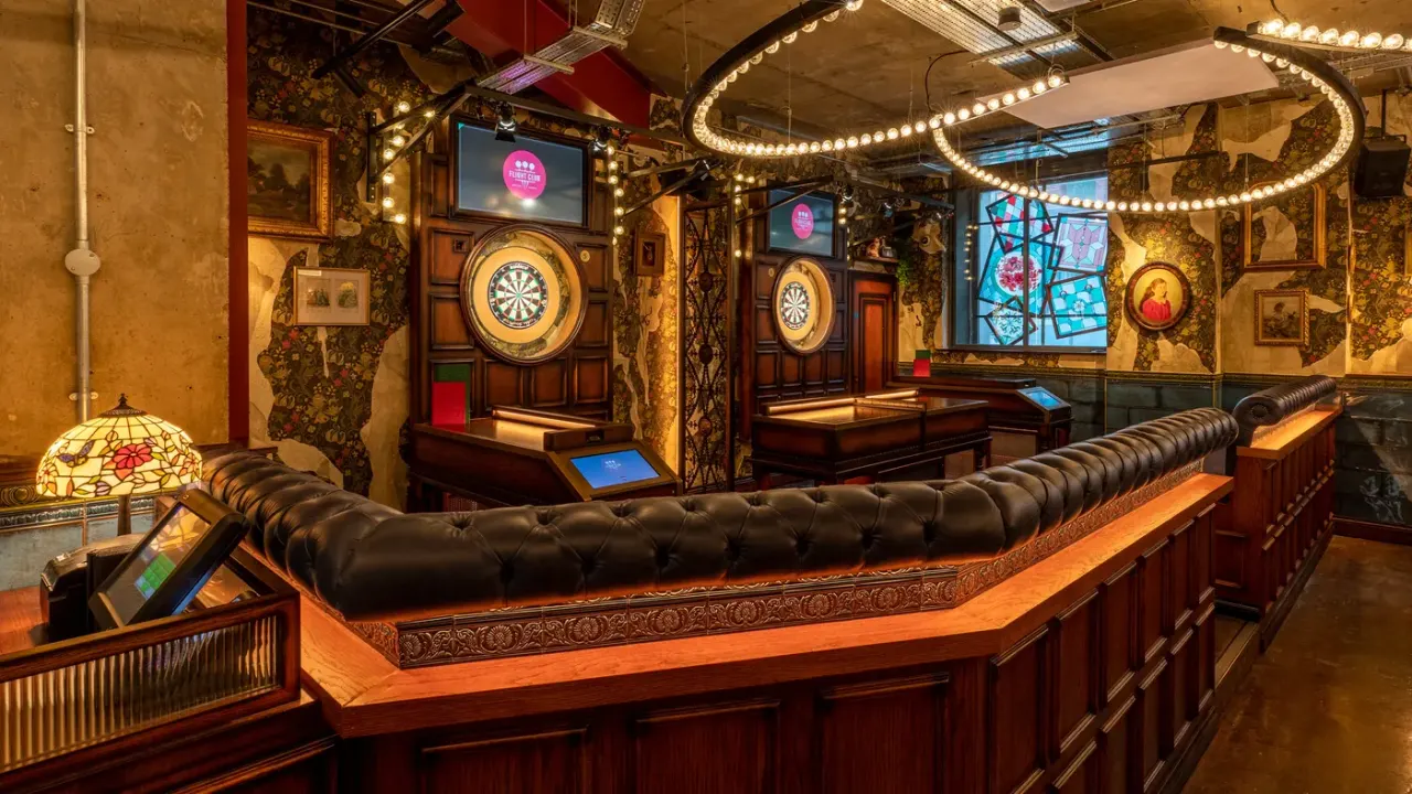 Luxurious indoor entertainment space with dartboards, leather seating, neon signage, and vintage décor.