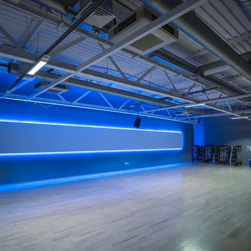 Modern industrial space with bright blue neon strip lighting along walls and wooden flooring.