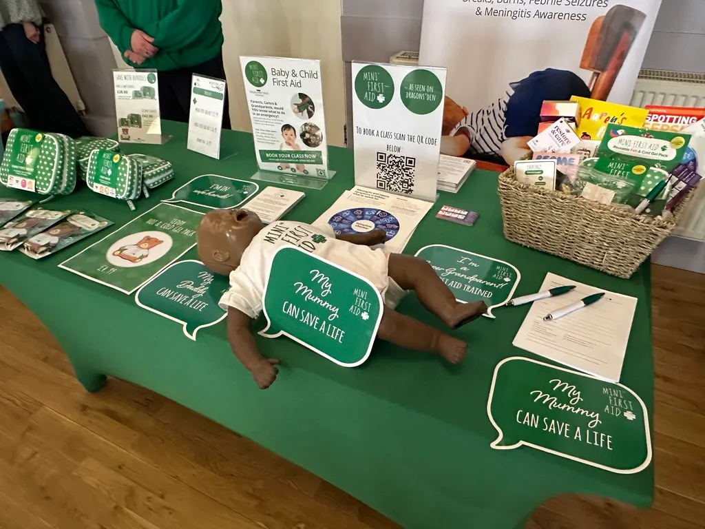 A baby lies on a green table surrounded by first aid and health awareness educational materials and leaflets.