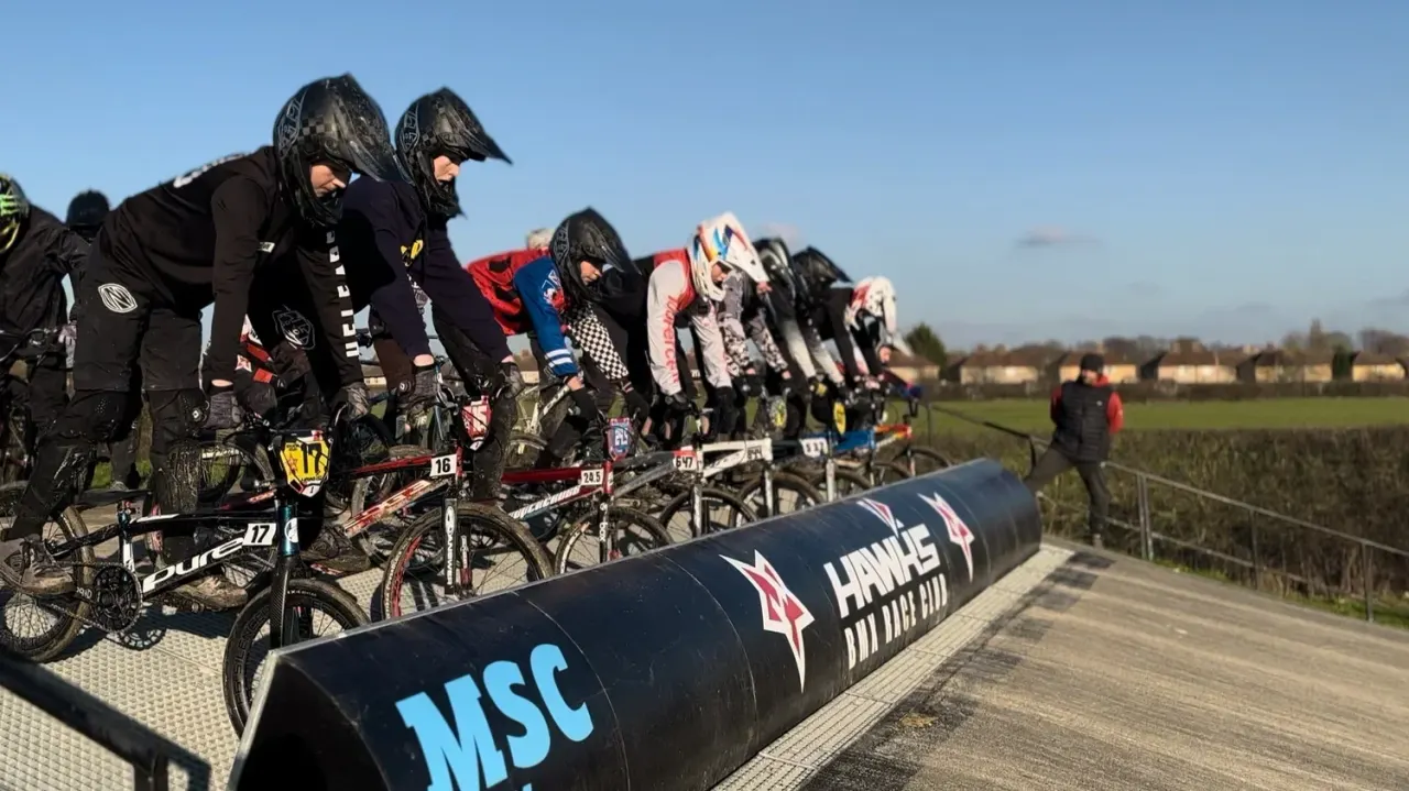 Young riders lined up at the starting gate on a BMX track, wearing helmets and protective gear, ready to race.