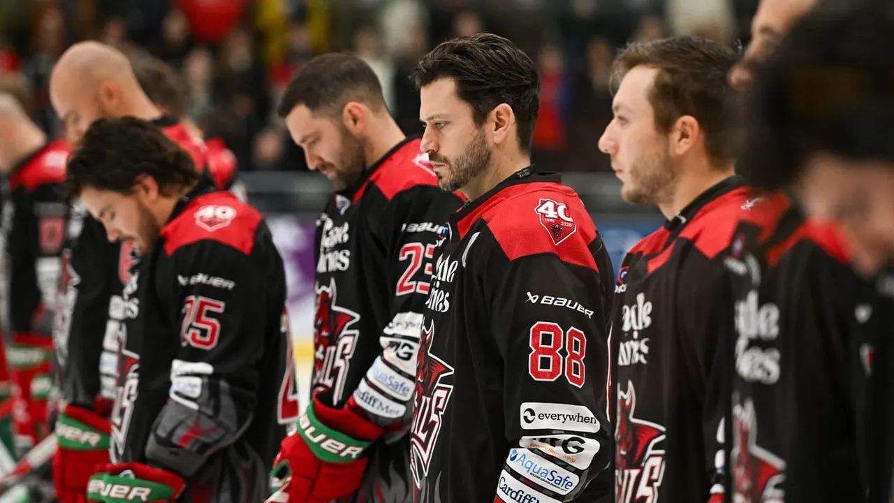 Ice hockey players in red and black team jerseys stand together during a match at an indoor arena.