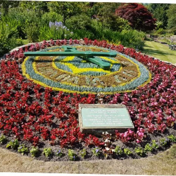 Ornamental flower bed with red flowers forming an eye design, surrounded by yellow, blue and green flowering plants, with a plaque at the base.