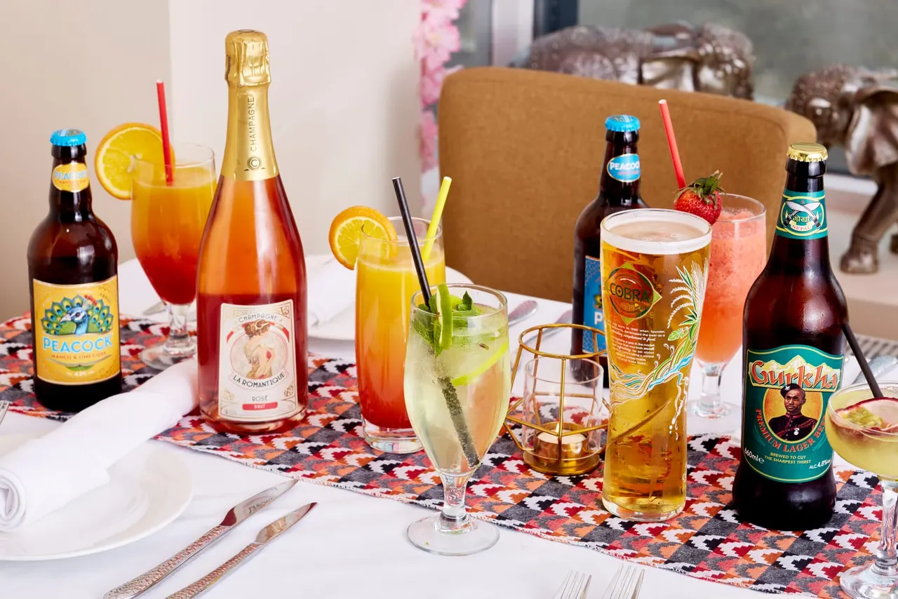 A formally set dining table with beer bottles, cocktails, champagne, and colourful mixed drinks garnished with citrus and berries.