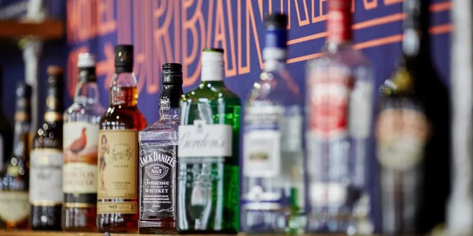 Various spirits and alcoholic bottles displayed on a bar counter with blurred signage behind.