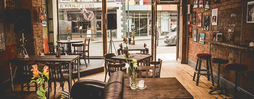 Interior of a vintage café bar with exposed brick walls, wooden tables and chairs, and musical instruments on display.