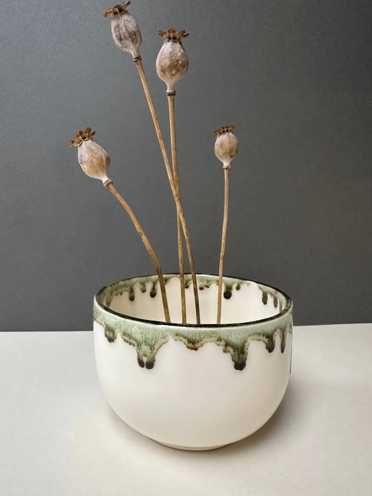 Dried poppy seed heads arranged in a ceramic bowl with green drip glaze.