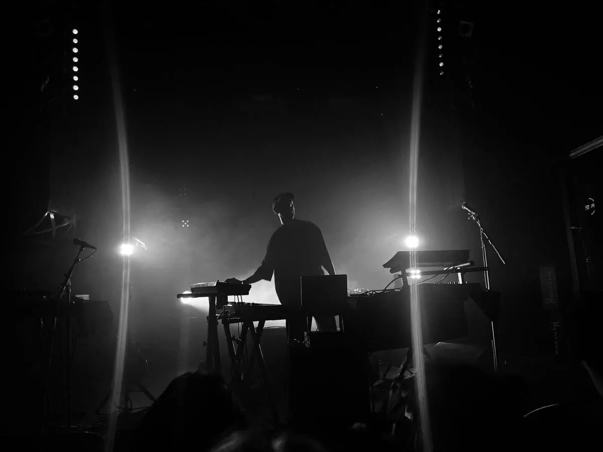 Musician performing at electronic keyboard on dimly lit stage with dramatic spotlight lighting.