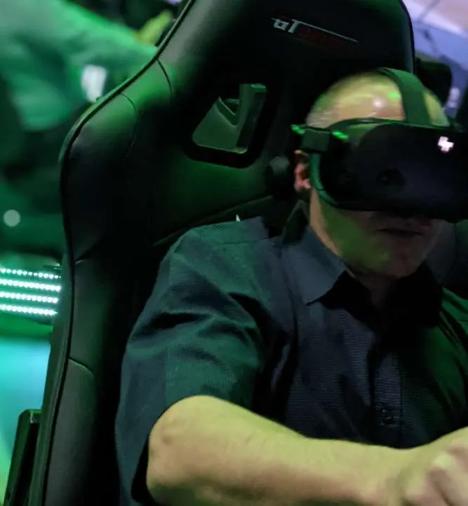 Person wearing VR headset whilst seated in a racing simulator with green lighting.