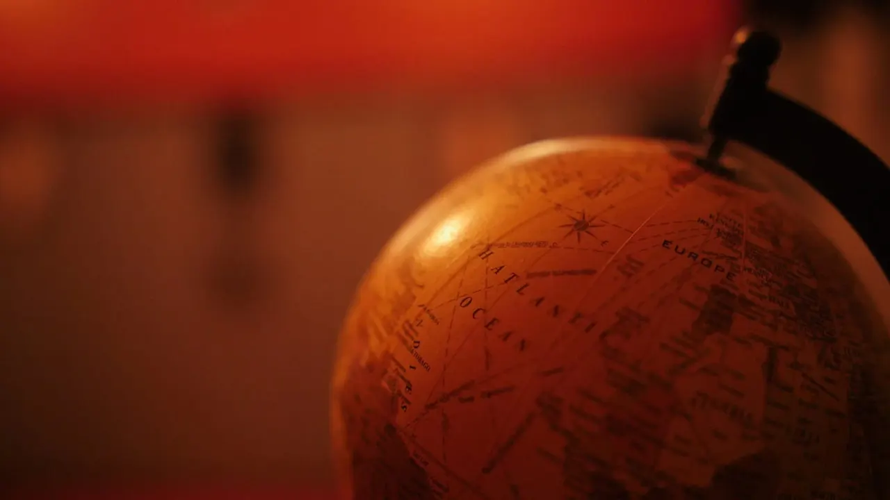 Close-up of a vintage globe with a silhouetted figurine perched on top against warm orange lighting.